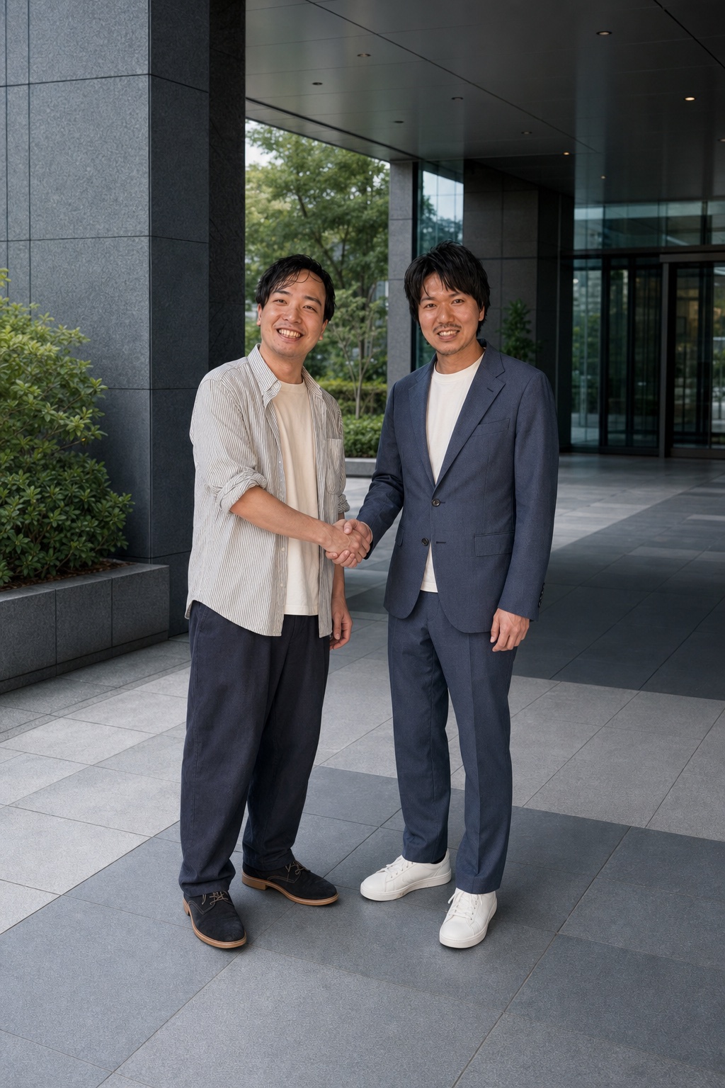 ビルのエントランス前で握手する株式会社オーパスワン 高久知丸さんとKAKUKATA 林英明
